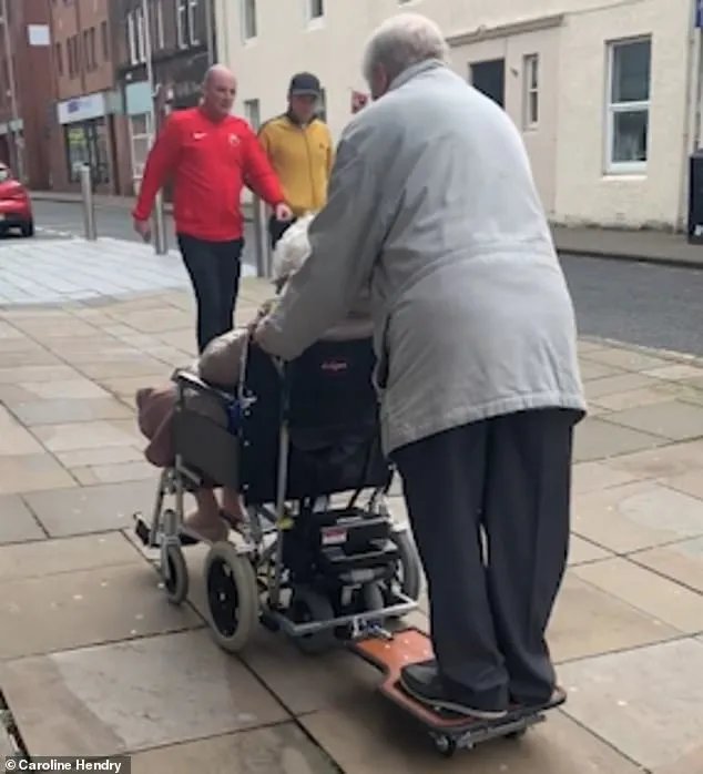 Elderly Husband Rides on Buggy Board Attached to His Wife’s Electric Wheelchair